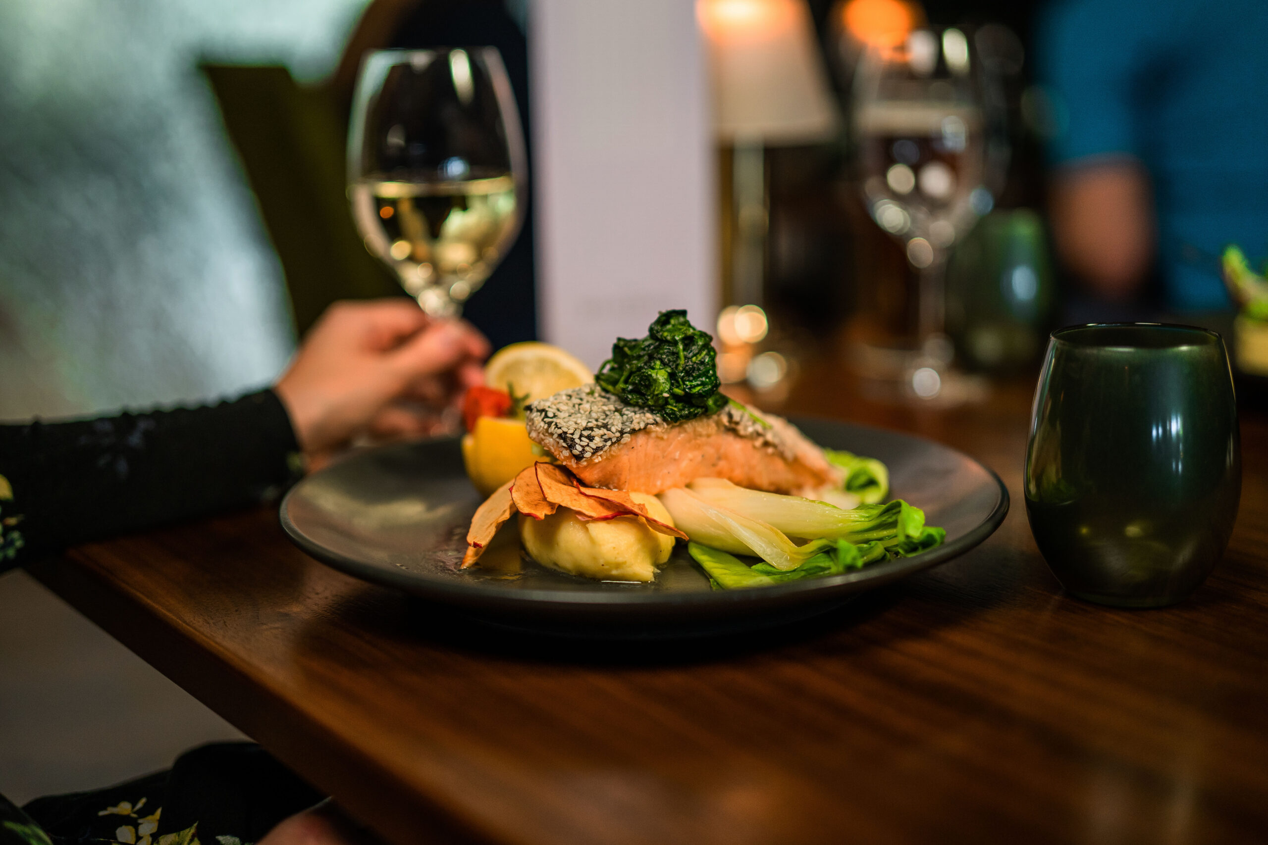 dish of salmon fillet with mixed vegetables and a glass of white wine in the background